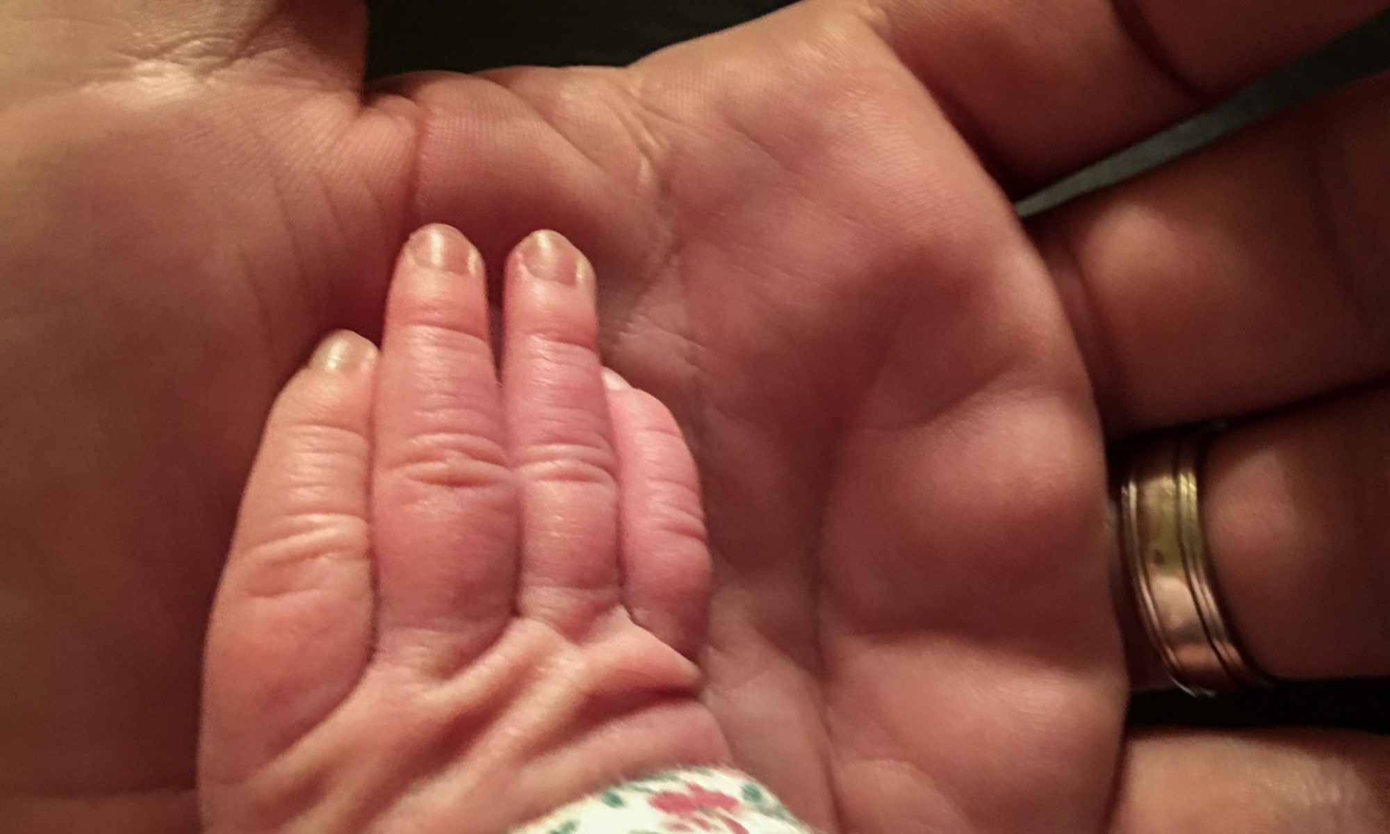 A baby's hand is pressed against a bigger father's hand.